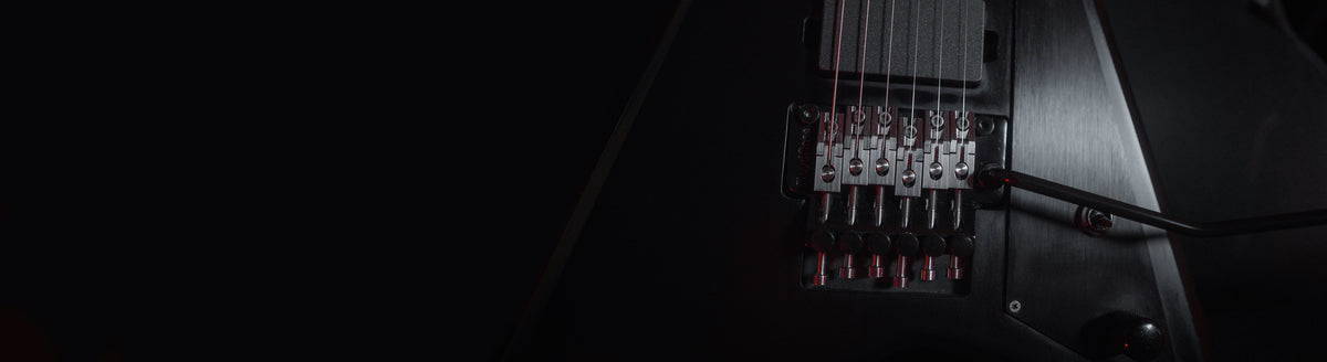 Black electric guitar and warm gold hardware in a dark guitar workshop